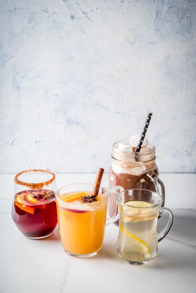 Té, café , jugo y chocolate en diferentes tazas de vidrio sobre mesa.