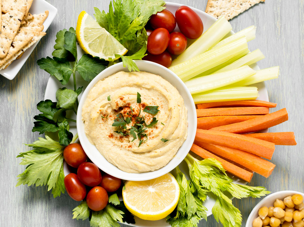 Plato con verduras en palitos bajo un cuenco de hummus con trocitos de especias.