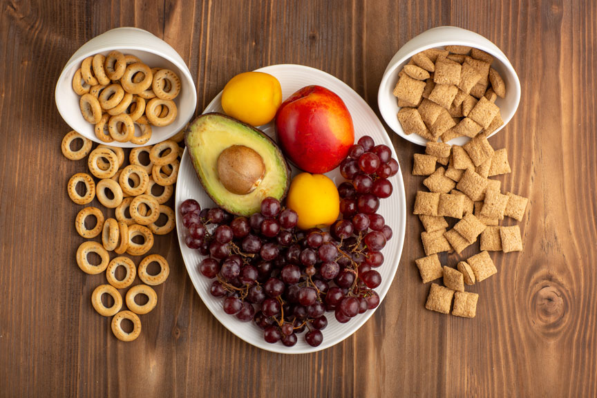 Fotografía de varias frutas en un plato con dos platitos adjacentes de cereales